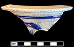 Gray-bodied salt glazed stoneware chamber pot with engraved motif outlined in cobalt-blue  under the glaze.  Cordoned rim. Chamber pots made for export to Britain and its colonies are generally decorated with two sprig molded lions and other simple stamped rosettes (Skerry and Hood 2009:52). 7.25&rdquo; rim diameter, from 18CV60.